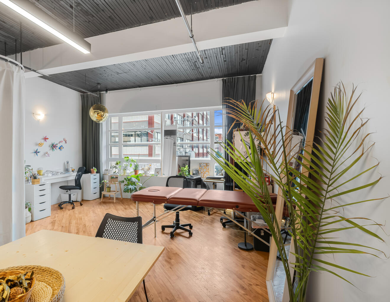 Grande pièce lumineuse avec espace de travail, plantes et fenêtres sur rue